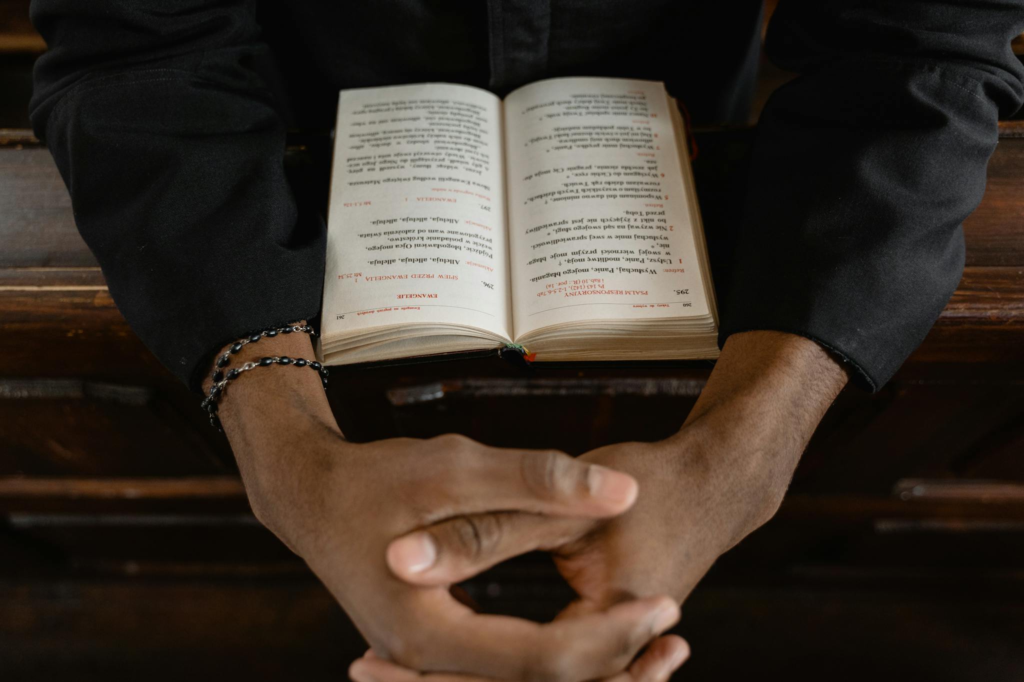 Close-up of hands clasped over an open Bible, symbolizing prayer and faith.